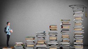 Eine Person steht vor mehreren Bücherstapeln.