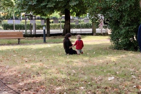 Eine Frau kniet auf einer Wiese. Ein Kind neben ihr zeigt ihr etwas.