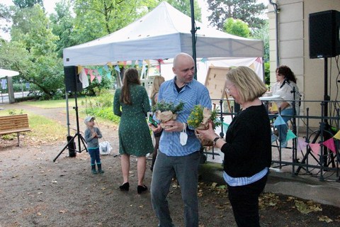 A man and a woman are talking outside. They are holding flowers in their hands. The sun is shining.