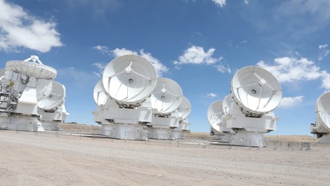 Wüstenboden, darauf weiße große Teleskope vor einem blauen Himmel mit Wolken
