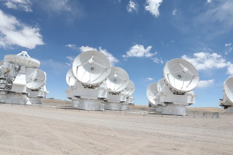 Wüstenboden, darauf weiße große Teleskope vor einem blauen Himmel mit Wolken