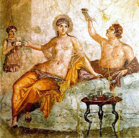 Symposiumsszene auf einem antiken Fresko aus Herculaneum. Wall painting depicting a banquet. A man drinks from a type of drinking vessel with two openings called a rhyton. His female companion wears a sheer garment and a golden net over her hair. A female servant attends to the couple, proffering a small box. The table in front holds a set of silver vessels for mixing wine. The whole scene represents an idealized Greek drinking party, a pleasurable sight for the guests of this first century Roman household. 
