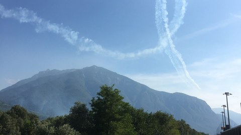 Fahrradweg mit Blick auf einen Berg. Darüber hat ein Flieger ein Looping in den Himmel gezeichnet.