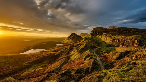 Zu sehen ist eine in warmes sonnenuntergangslicht getauchte Hügellandschaft.