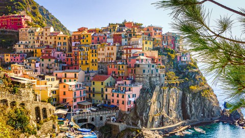 Zu sehen sind sich an einem Felsen am Meer aufreihende bunte Häuser. Sie gehören zu Cinque terre, einem Küstenstreifen der Italienischen Riviera