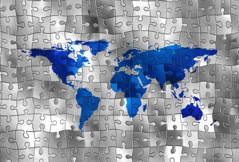 Zu sehen ist ein Puzzle mit dunkelblauer Weltkarte vor silbernem Hintergrund