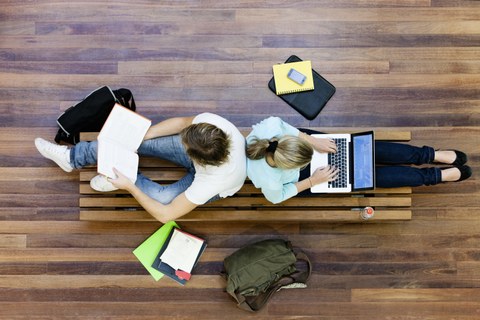 Zwei Studierende sitzen mit Büchern und Laptop am Fußboden