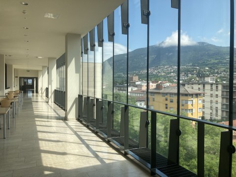 Flur im trienter Fakultätsgebäude mit Tischen entlang einer Glasfront, dahinter der Blick über die Stadt und die Berge
