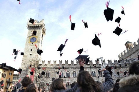 Impression der Abschlusszeremonie in Trento. Die typischen, viereckigen Abschlusshüte werden in die Luft geworfen. Im Hintergrund die Kulisse des trentiner Doms.