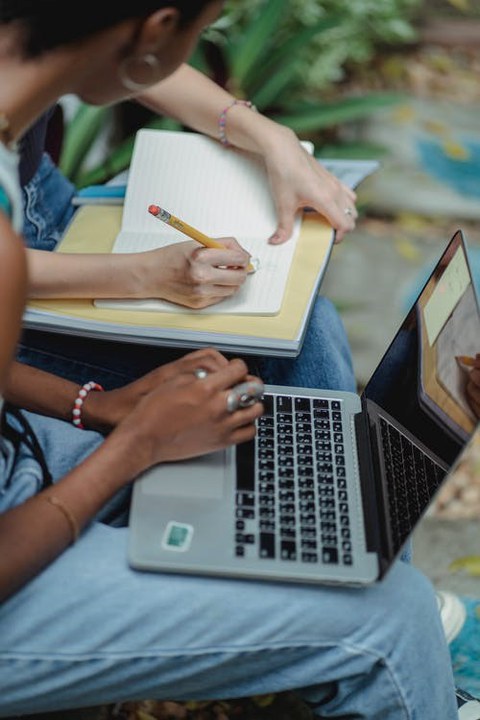 zwei Personen nebeneinander sitzend mit Zetteln und Laptop