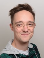 Ein junger Mann mit runder Brille lächelt in die Kamera.