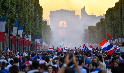 Das Foto zeigt eine Demonstration. Es sind rechts und links sowie unter den Demonstrant:innen viele französische Flaggen zu sehen.