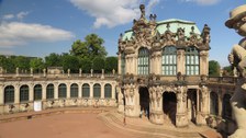 Das Foto zeigt die Innenfassade des Dresdener Zwingers. Sie ist mit vielen Ornamenten verziert. Auf dem Geländer der Fassade und dem Dach des Gebäudes erkennt man viele Skulpturen.