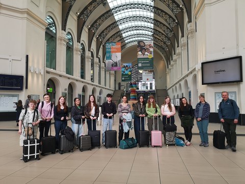 Gruppe Studierender und Professoren mit Reisekoffern auf dem Bahnhof