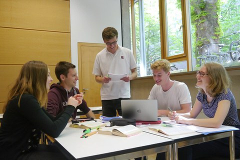 5 Studentinnen und Studenten, die in einem Seminarraum angeregt diskutieren