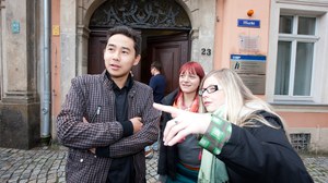 Foto mit drei jungen Leuten, einem Mann und zwei Frauen, die vor dem IHI Haupteingang stehen.