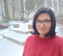 Zu sehen ist Ritu George Kaliden im Profil im Vordergrund. Der Hintergrund ist ein mit Schnee bedeckter Gebäudevorplatz.