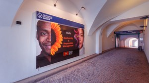 Blick in die historische Einfahrt des Hauptgebäudes des IHI Zittau mit Rundgewölbe. Man blickt auf ein großes Schild an der Wand, welches internationale Studierende und das Logo des IHI Zittau zeigt.