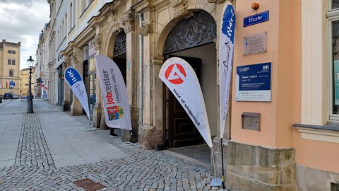 Fahnen der IHK Dresden und des Jobcenters Görlitz laden vor dem Haupteingang des IHI Zittau zur Arbeitgeberkonferenz ein