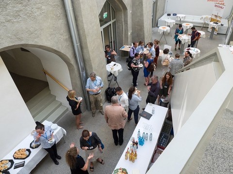 Pausengespräche im Denksalon: Blick von oben auf ein Foyer im Schlesischen Museum Görlitz, in dem das Buffet sowie Besucher, die miteinander sprechen, zu sehen sind.