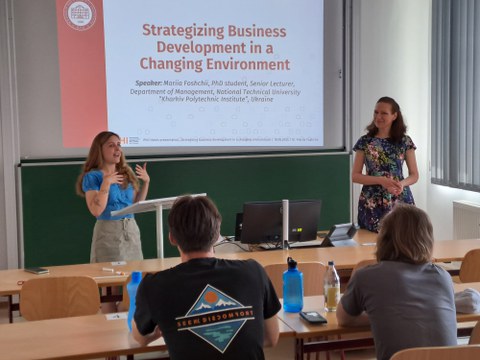 Mariia Foschchij von der TU Kharkiv während ihres Vortrags. Hinter ihr ist eine Power-Point-Präsentation zu sehen, im Vordergrund Studierende, die zuhören.