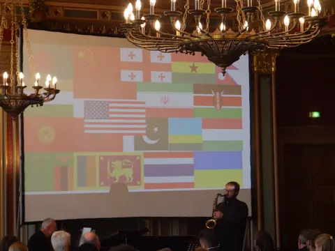 Ein Saxofonist vor einer Videoprojektion mit vielen Länderflaggen
