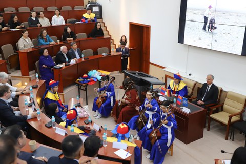 Prof. Karsten Wesche bei der Zeremonie zur Verleihung der Ehrendoktorwürde der Mongolischen Nationaluniversität. Zu sehen ist ein Hörsaal mit Publikum und ein Orchester in traditioneller mongolischer Kleidung.