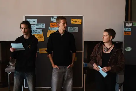 Teilnehmende des Projekts Youth Vision Action während eines Workshops. Im Hintergrund steht eine Pinwand mit Arbeitszetteln.
