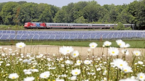 A train passing by solar panels and nature