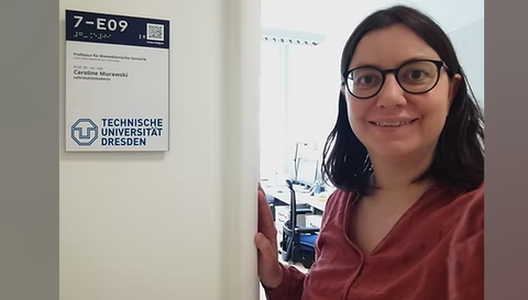 Frau Caroline Murawski mit einem strahlenden lächeln vor Ihrem neuen Büro an der Technischen Universität Dresden.