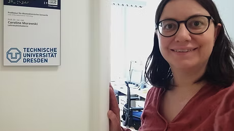 Frau Caroline Murawski mit einem strahlenden lächeln vor Ihrem neuen Büro an der Technischen Universität Dresden.