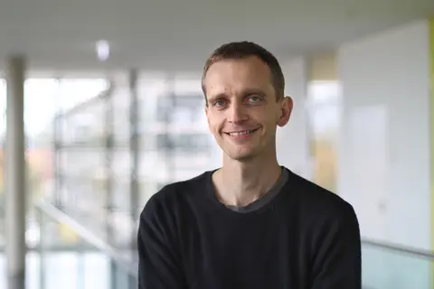 Felix Schmieder lächelt in die Kamera. Er trägt einen schwarzen Pullover.