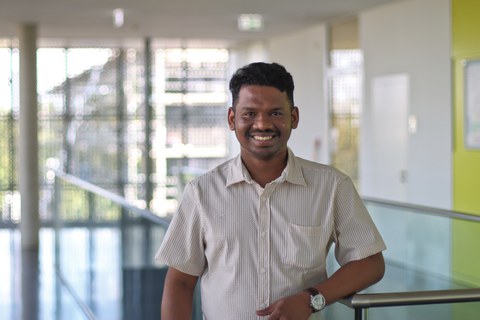 Sudhi Mahadevan wears a verticall striped shirt with a decent white-orange color pattern. We smiles to the camera.