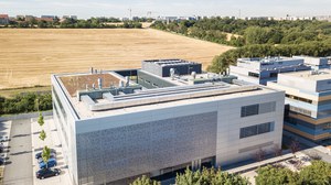 Luftaufnahme des Werner-Hartmann-Baus mit silbernem Gebäude mit mikrostrukturandeutender Fassade vor einem goldleuchtenden Weizenfeld