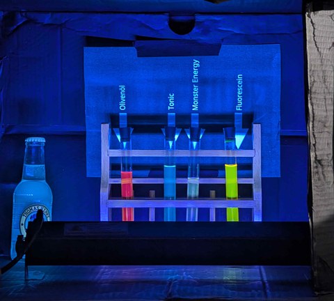 Eine UV Lampe leuchtet Flüssigkeiten mit organischen Molekülen an. Durch die besondere Strutkur von Molekülen in Olivenöl, Tonic, Monster Energy und Fluorescein leuchten die flüssigkeiten jeweils Rot, Türkis, Gelb und Grün.