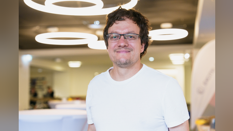 The person Robert Kuschmierz wears a white shirt and glasses. He has brown hair and smiles directly into the camera.