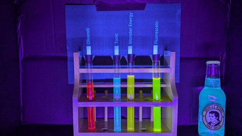 Die drei Haushaltsüblichen Stoffe Olivenöl, Tonic Water und ein Energy Drink sowie Fluorescein werden mit UV Licht angeleuchtet. Dadurch leuchten die flüssigkeiten in den Reagenzgläsern Rot, Blau, Gelb und Grün auf.