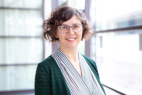 Agnė Žukauskaitė smiles into the camera. She wears a dark green cardigan with a formal, suit-like blouse