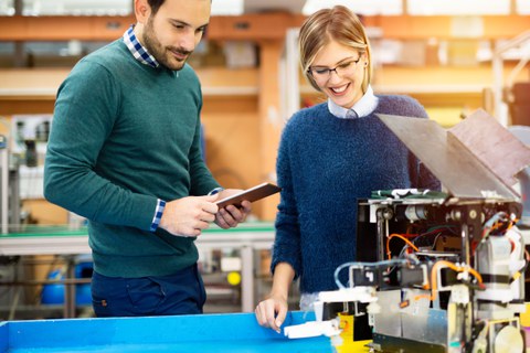 Bild: eine junge Frau und ein junger man stehen vor einem Tisch, auf dem ein Roboterprojekt ausgebreitet ist. 