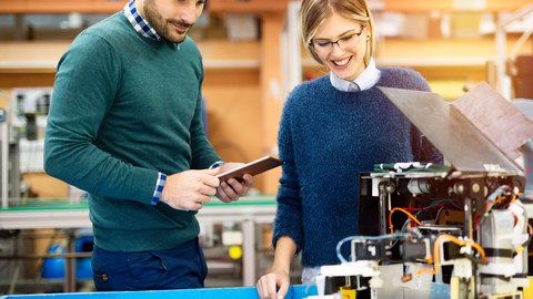 Bild: eine junge Frau und ein junger man stehen vor einem Tisch, auf dem ein Roboterprojekt ausgebreitet ist. 