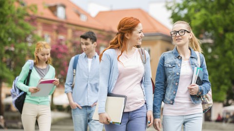 Bild: vier junge Menschen laufen und reden in Paaren miteinander. Sie haben (vermutlich) Lernunterlagen dabei. Sie sehen aus, als ob sie nach der Vorlesung aus einem Uni-Gebäude ausgehen würden.