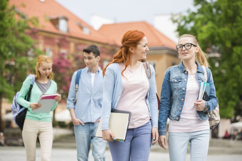 Bild: vier junge Menschen laufen und reden in Paaren miteinander. Sie haben (vermutlich) Lernunterlagen dabei. Sie sehen aus, als ob sie nach der Vorlesung aus einem Uni-Gebäude ausgehen würden.