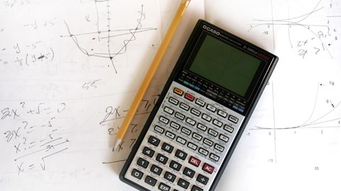 Ein Taschenrechner und ein Bleistift liegen auf einem Blatt Papier mit Formeln.