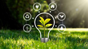 Glühbirne umrandet mit Symbolen zur Energie auf grünem Rasen