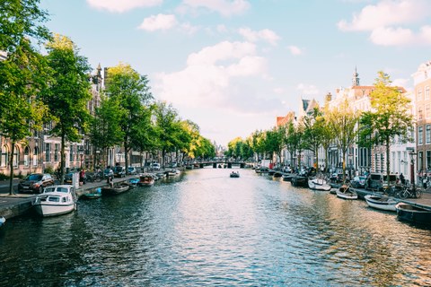 Ein Kanal in Amsterdam mit Booten und Bäumen und Häusern am Ufer