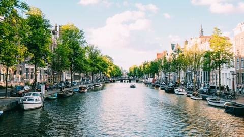 A canal in Amsterdam with boats and trees and houses on the shore
