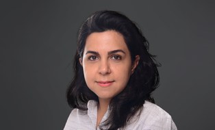 Woman with black hair and dressed in light blouse against dark background