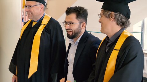 Lachender Absolvent zwischen Studiendekan und Prof. Uwe Aßmann
