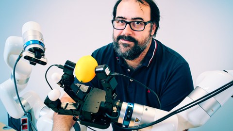 Prof. Robert Calandra mit zwei Roboterarmen, welche eine  Roboterhand mit ergriffener Zitrone und eine Kamera tragen