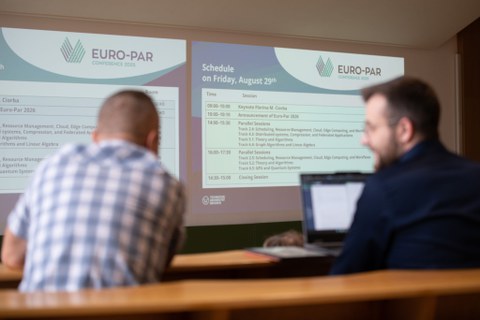 im Vordergrund unscharf zwei Personen mit Blick auf das Programm der EURO PAR 2025,